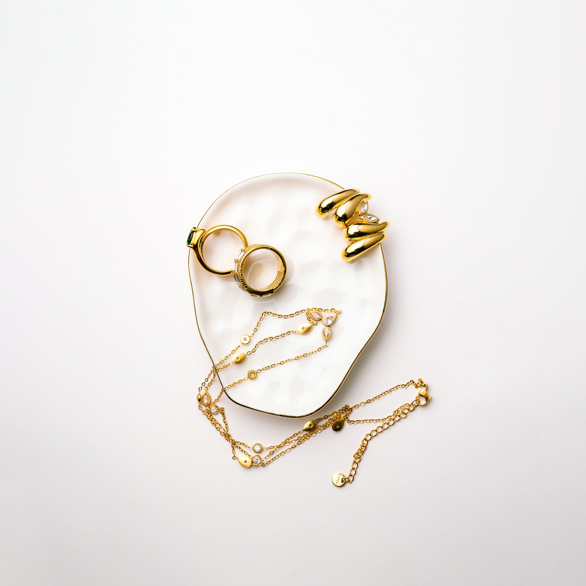Gold jewelry including rings and a necklace on a white surface