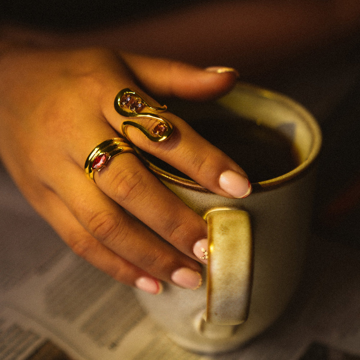 Hand holding a mug with gold rings on fingers, warm lighting
