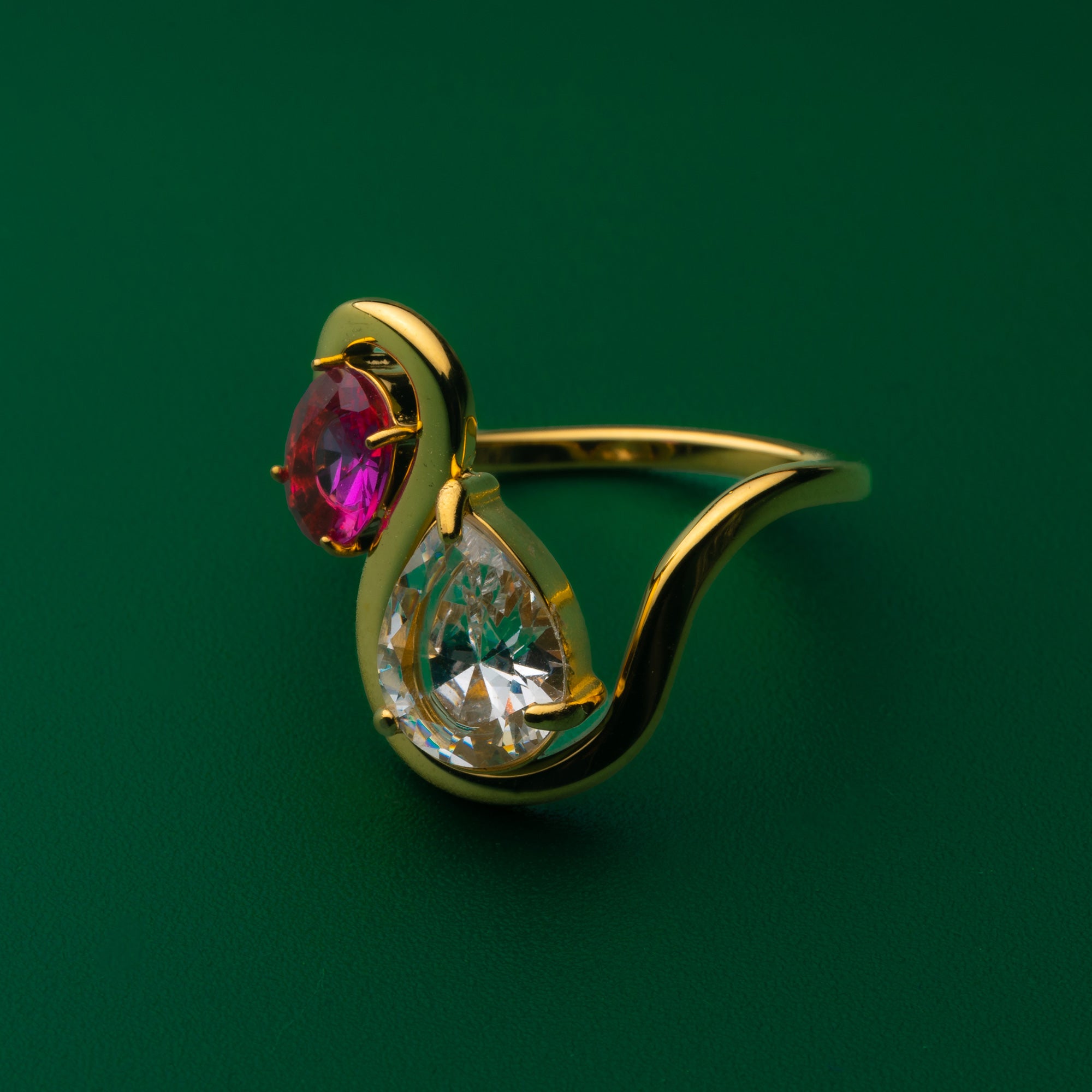 Amara Gold ring with a red gemstone and clear teardrop gemstone on a green background