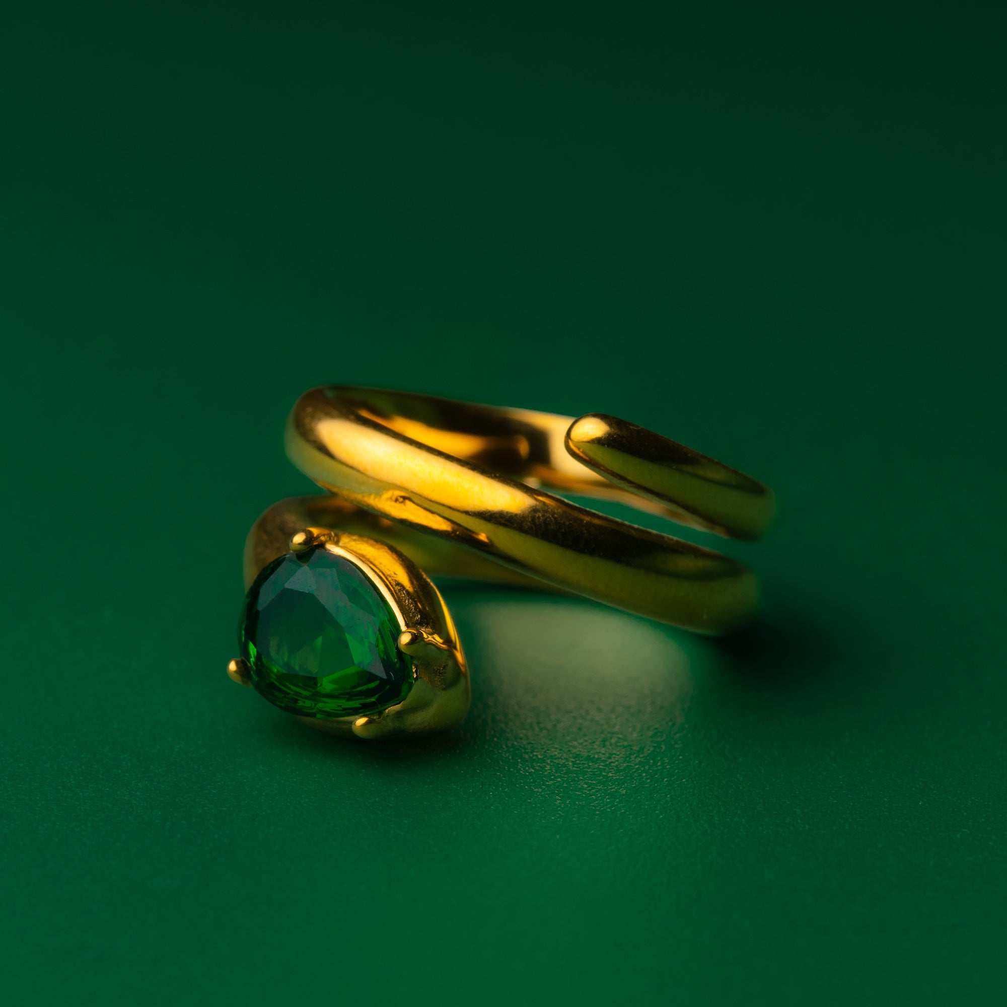 Ariana diamond gold ring with a green gemstone on a green background