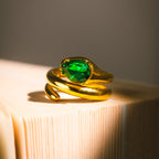 Gold ariana diamond snake-shaped ring with a green gemstone on a textured surface