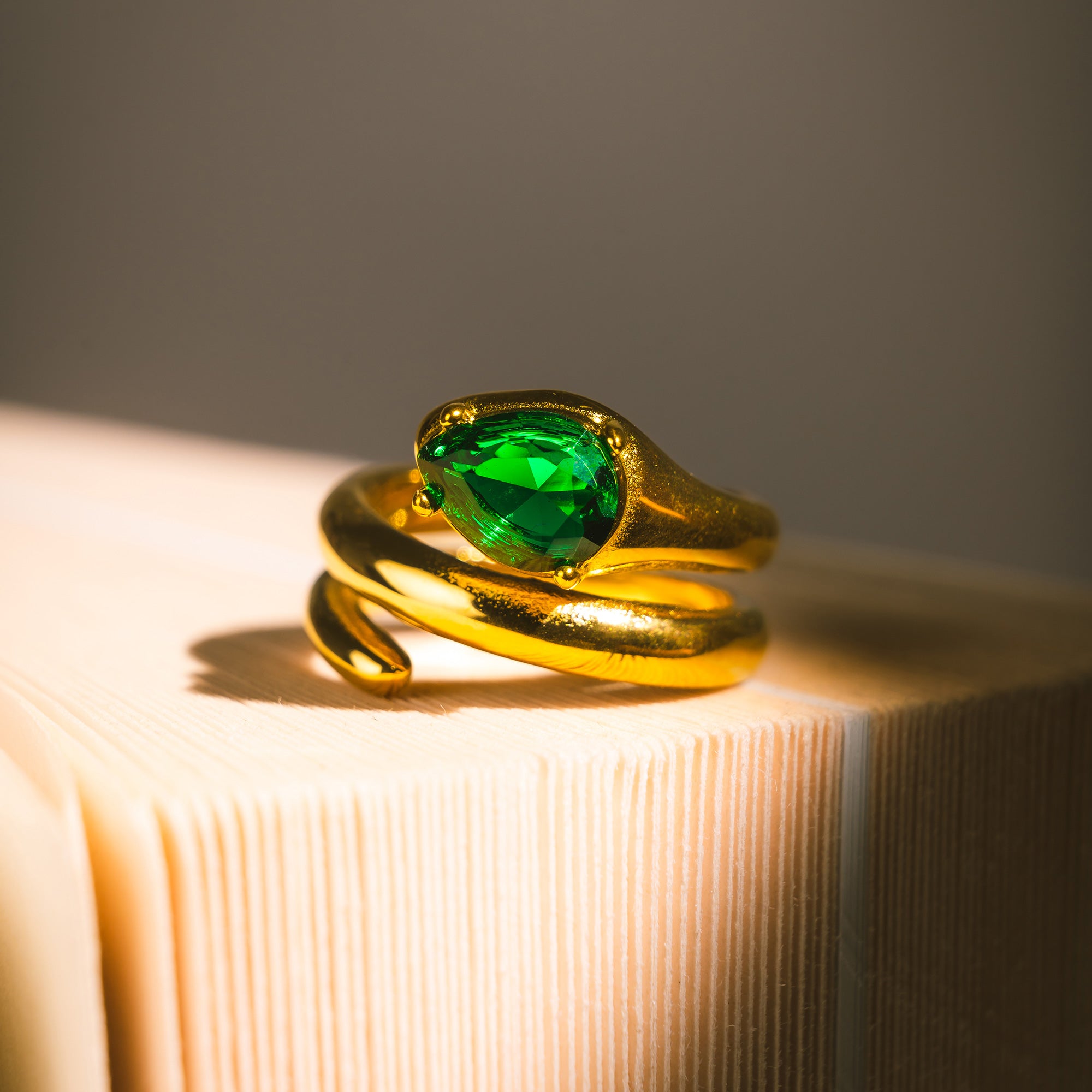 Gold ariana diamond snake-shaped ring with a green gemstone on a textured surface