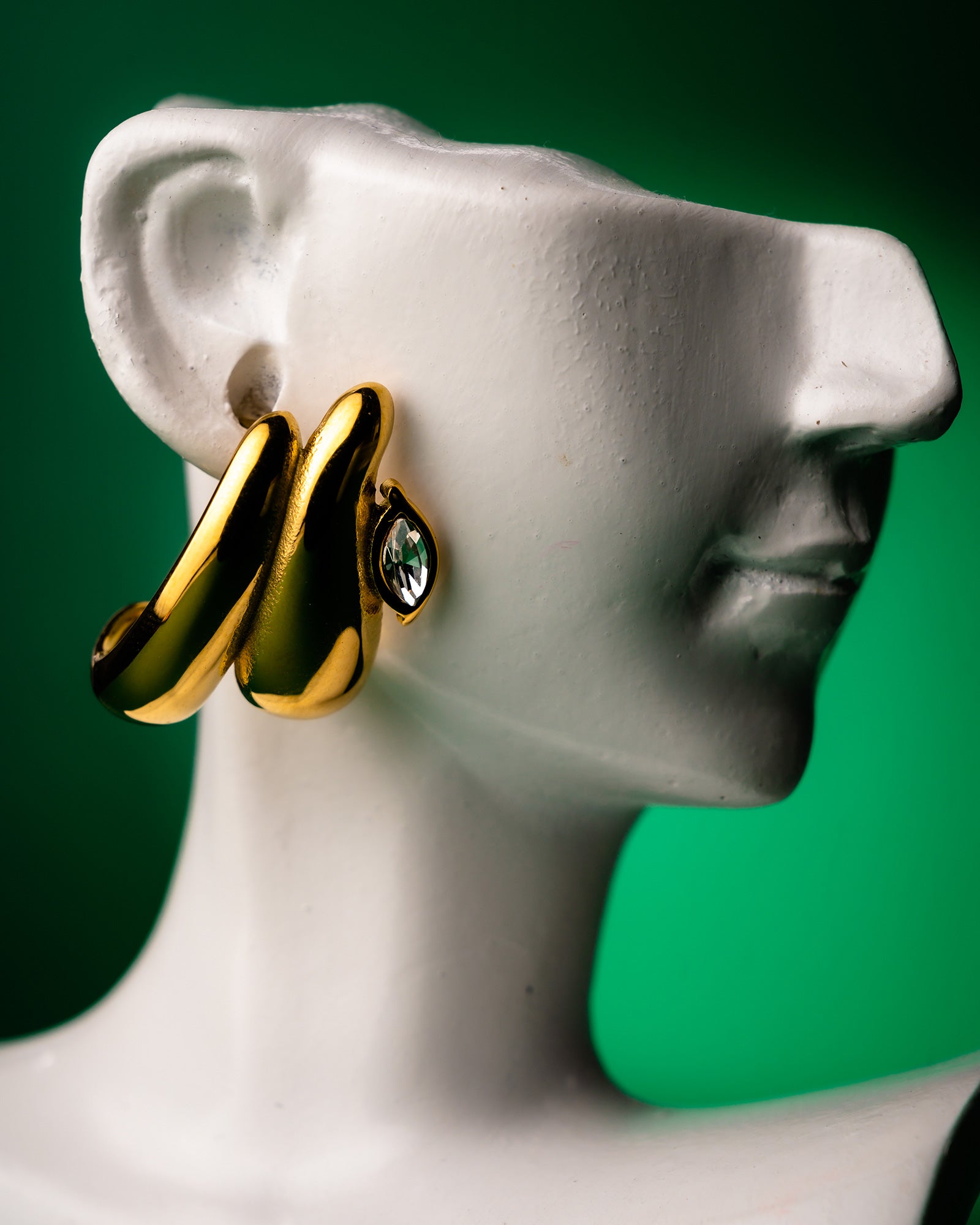Gold double teardrop earring on a mannequin ear with a green background