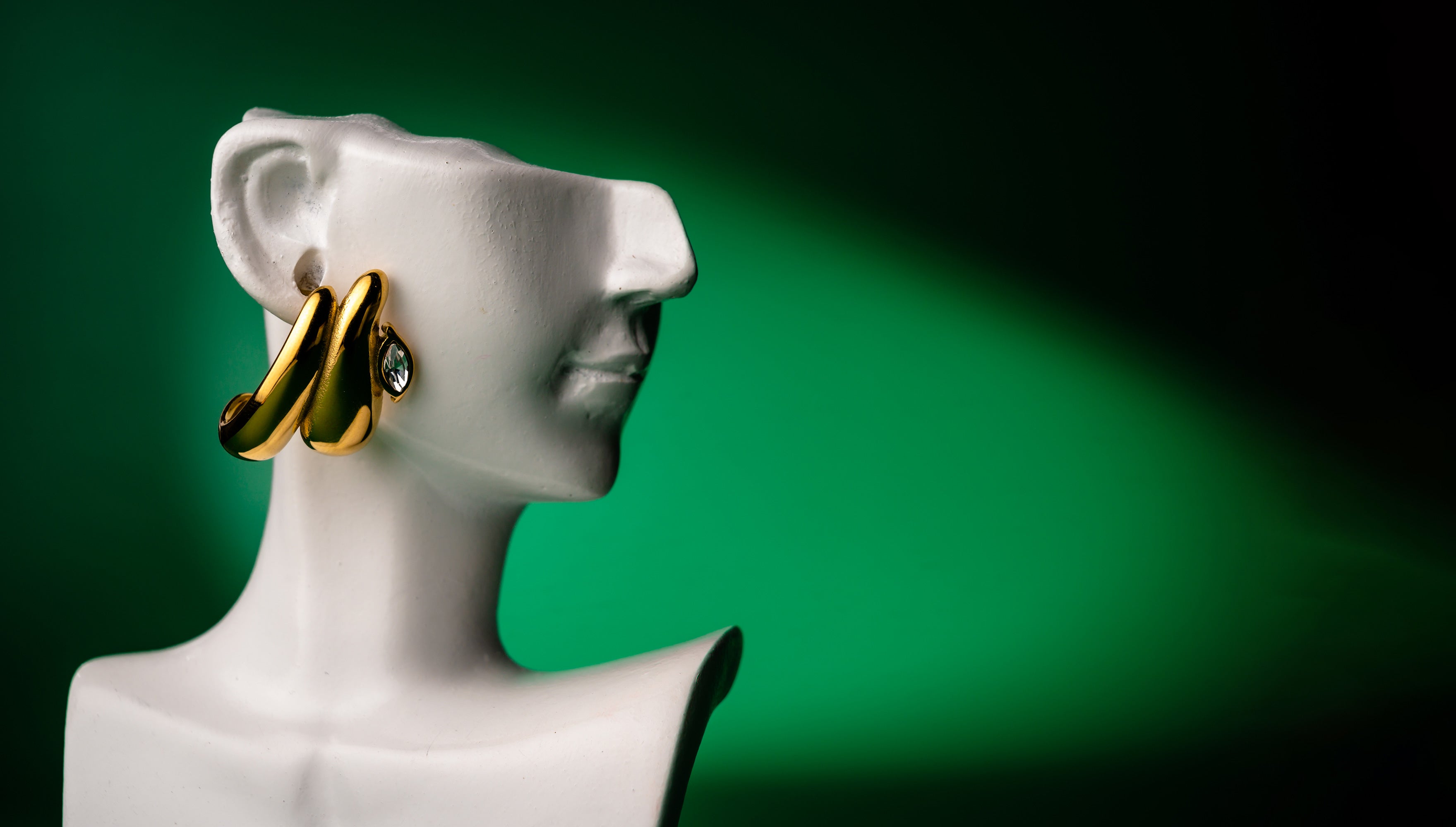 Gold  double teardrop earring on a white mannequin against a green background