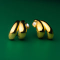 Double teardrop gold hoop earrings with embedded stones on a green background