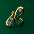 Golden line wave ring with gemstones on a green background