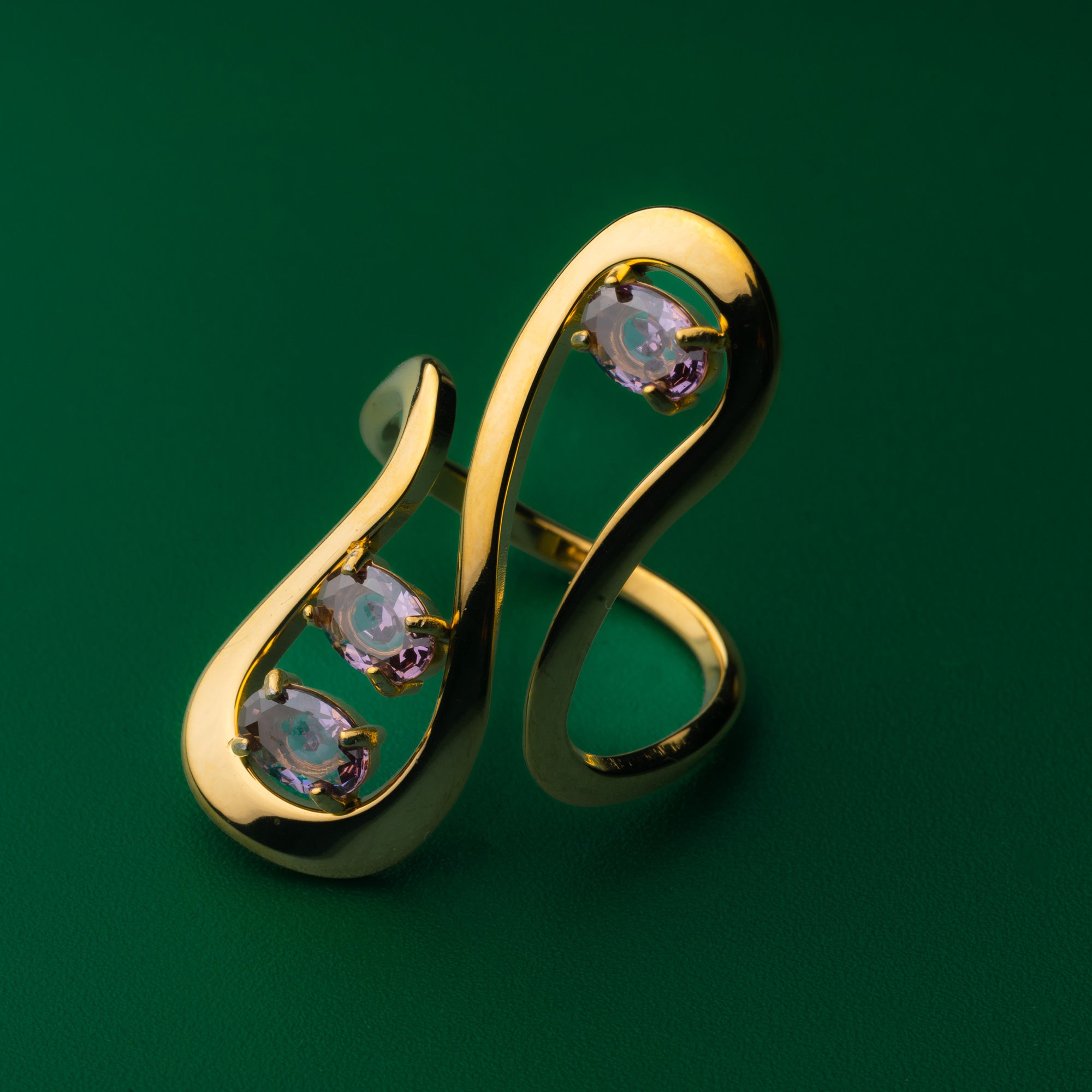 Golden line wave ring with gemstones on a green background