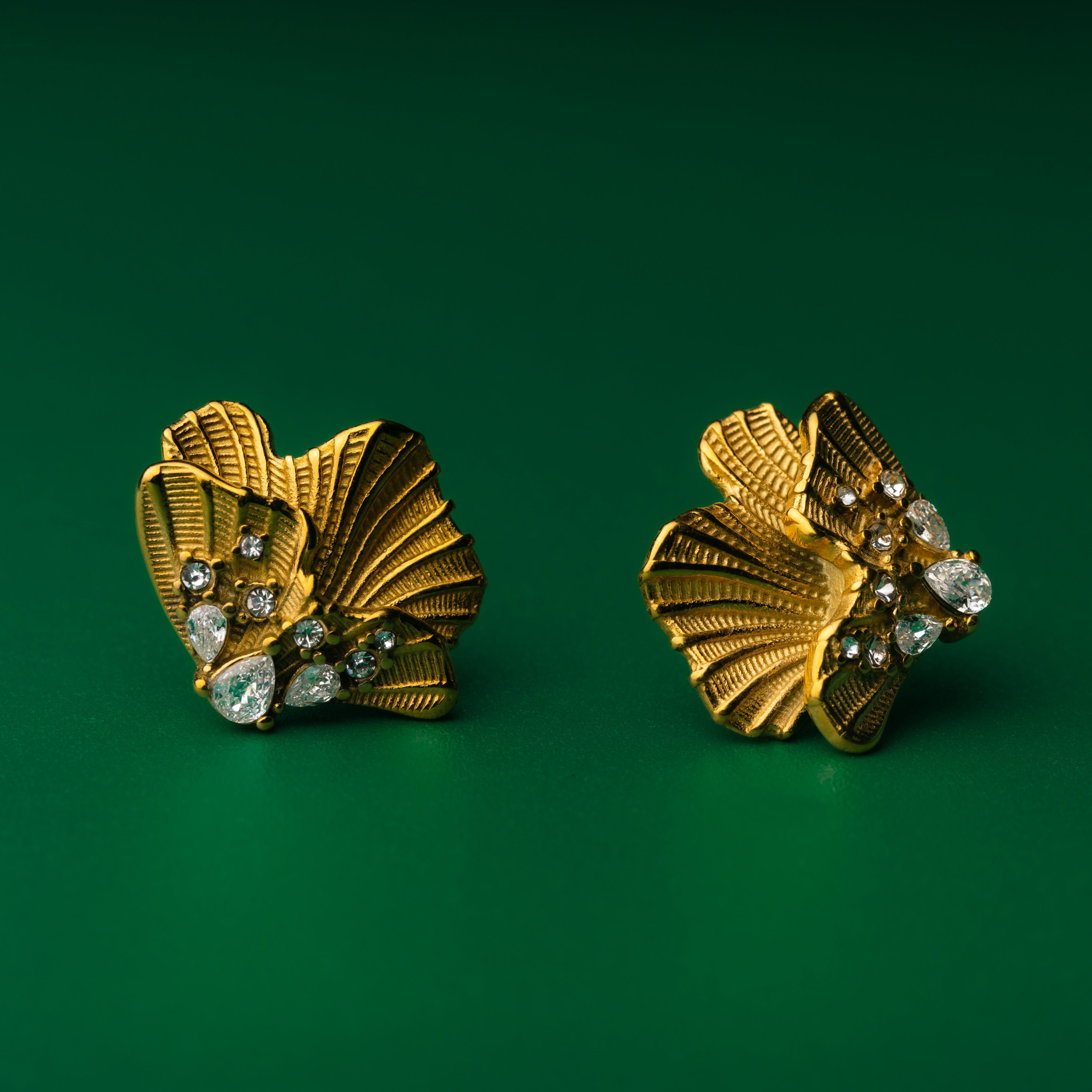 Pair of gold earrings golden shell studs earrings with gemstones on a green background