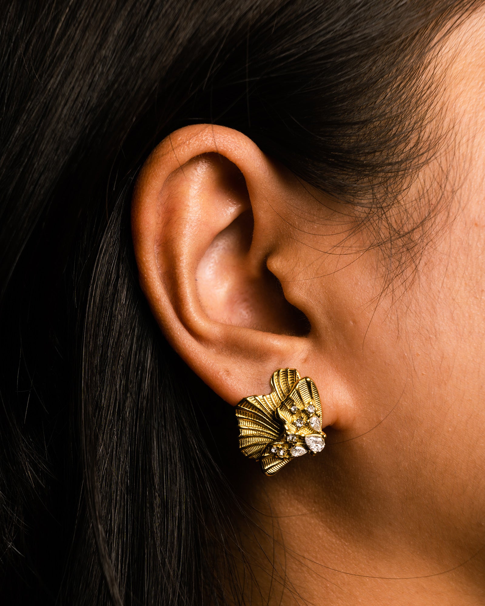 Gold golden shell studs earring worn by a person with dark hair