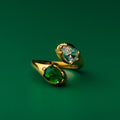 Green envy gold ring with green gemstone and clear gemstone on a green background