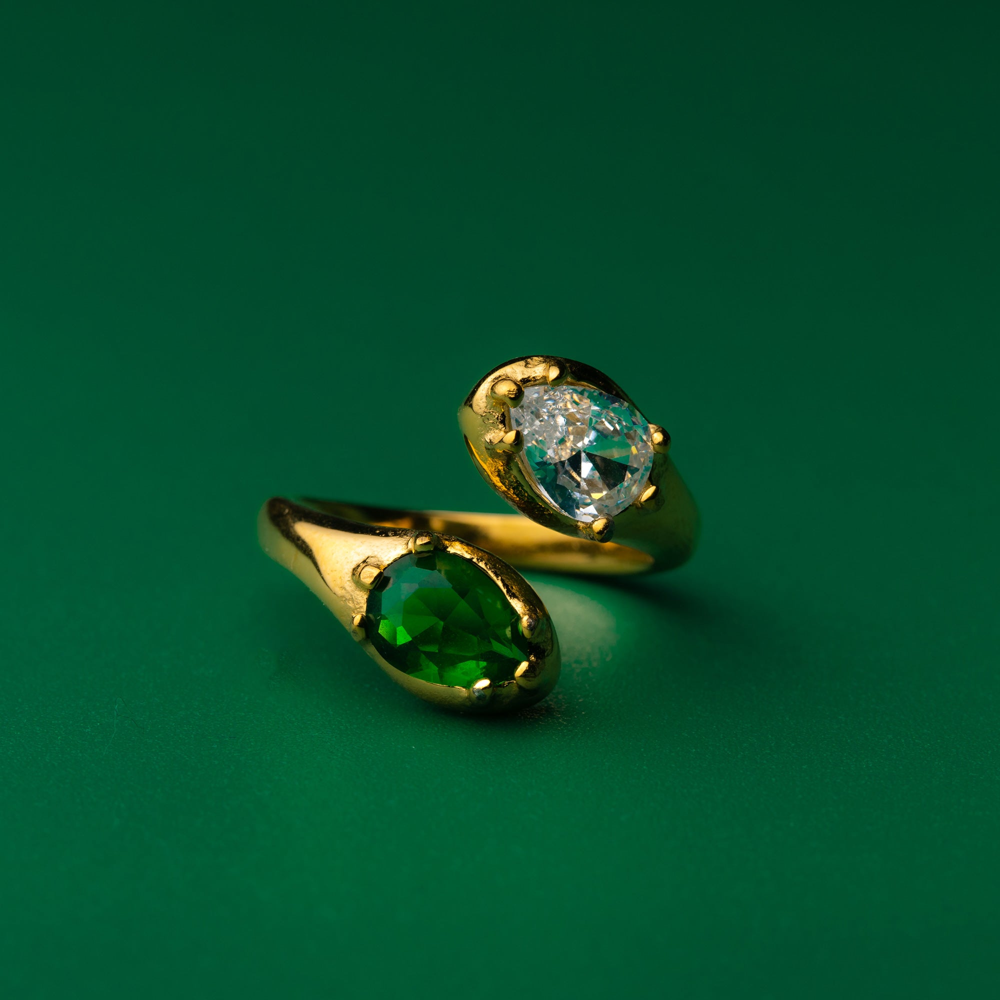 Green envy gold ring with green gemstone and clear gemstone on a green background