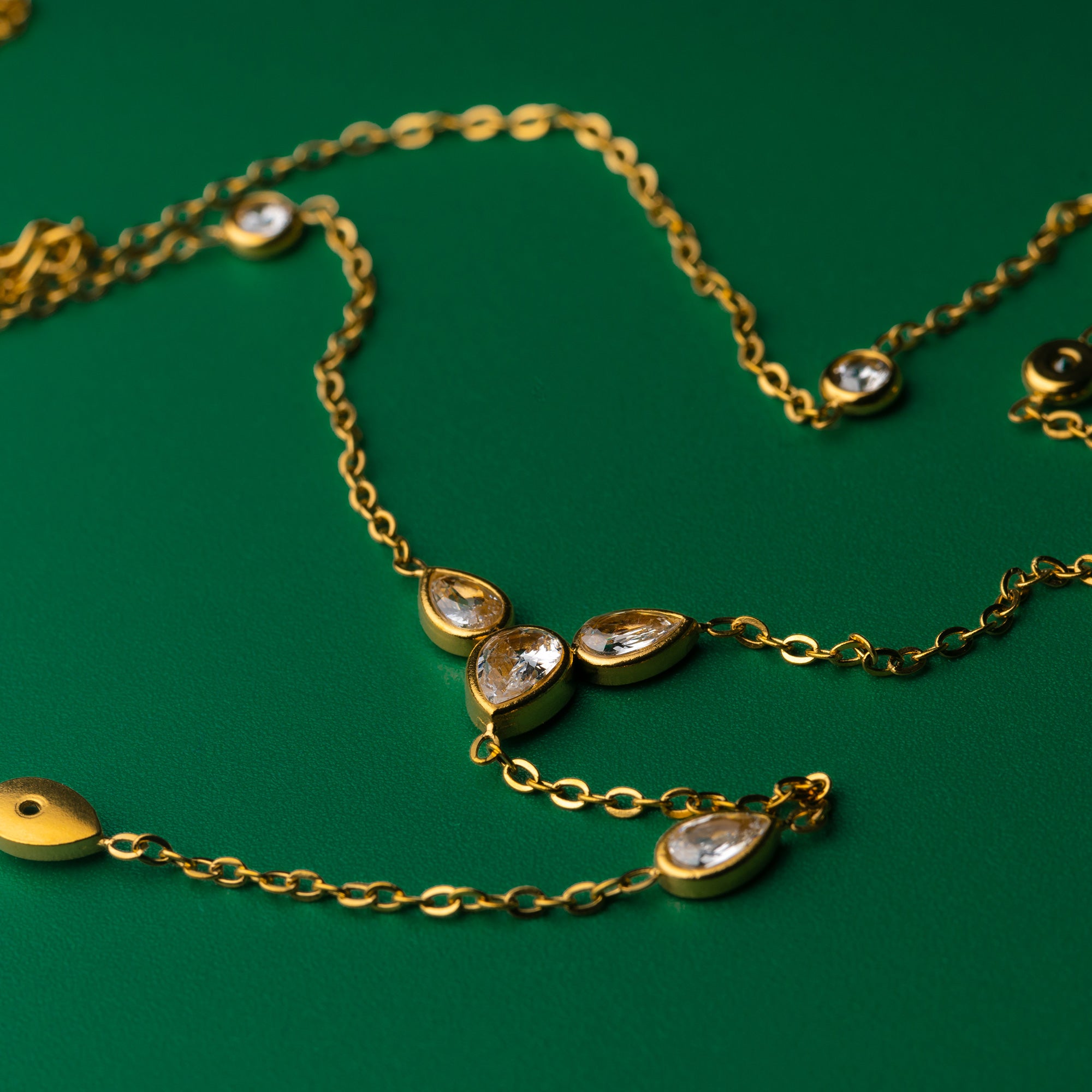 Lotus grace gold necklace with teardrop-shaped gemstones on a green background