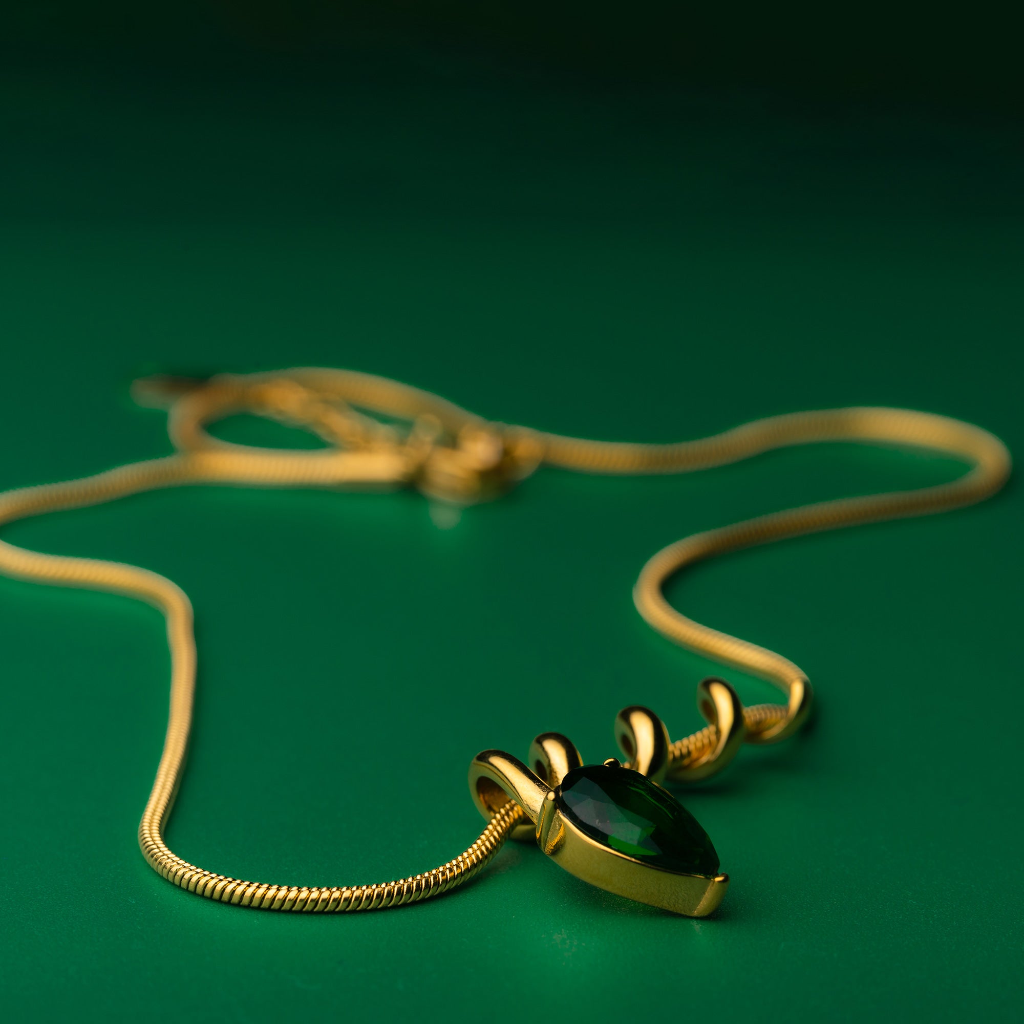 Midnight muse green gold necklace with a green gemstone pendant on a green background