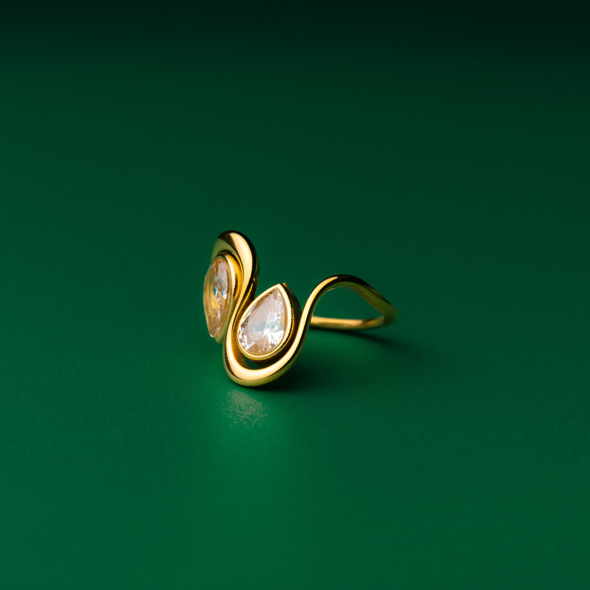 Teardrop goldring with two pear-shaped gemstones on a green background